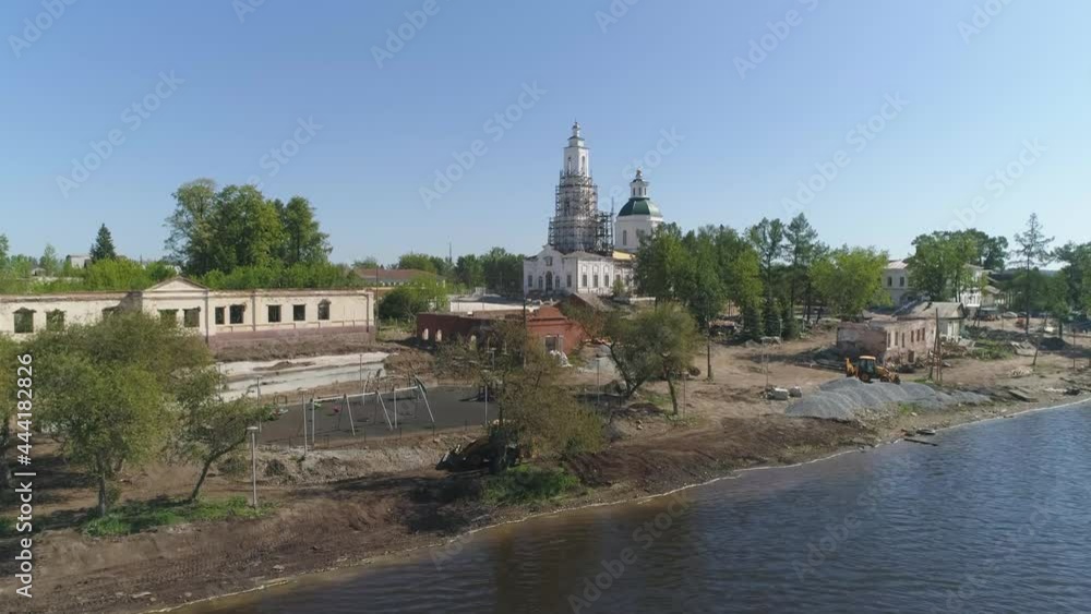 Aerial view of reconstruction of the area next to the church and pond in the provincial town. Reconstruction of the old church and old houses. Sports ground, Tractors and building materials on the sho Aerial view of reconstruction of the area next to the church and pond in the provincial town. Reconstruction of the old church and old houses. Sports ground, Tractors and building materials on the sho