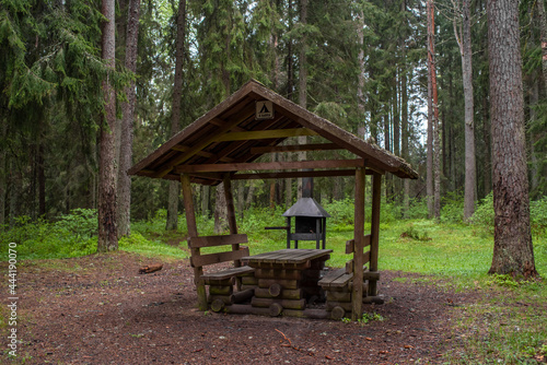 Public rest and barbeque RMK area in Estonian forest in Ida-Virumaa county on a cloudy summer day. Sign on the gazebo in Estonian - For four-person. Selective focus.