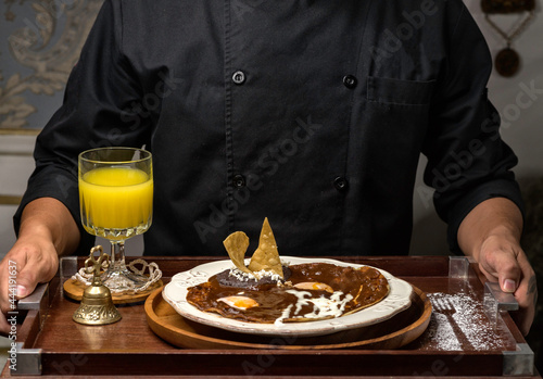 Desayuno especial de huevos rancheros con mole poblano y frijoles refritos sobre plato blanco y jugo de naranja.