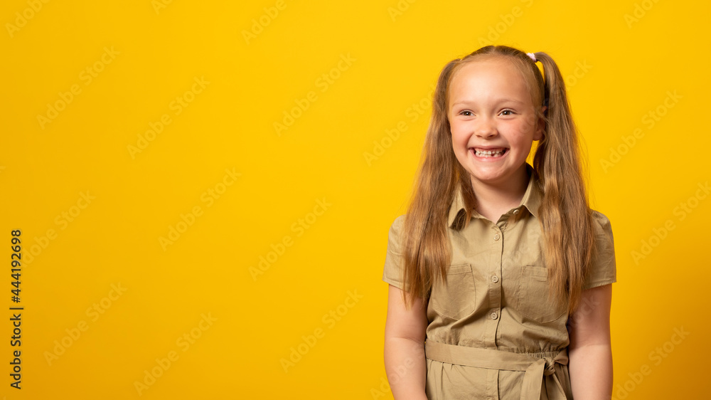 Banner, copy space. Happy little girl with two ponytails, dressed in a dress, smiling and laughing on a yellow background. Banner, copy space. Happy little girl with two ponytails, dressed in a dress, smiling and laughing on a yellow background.