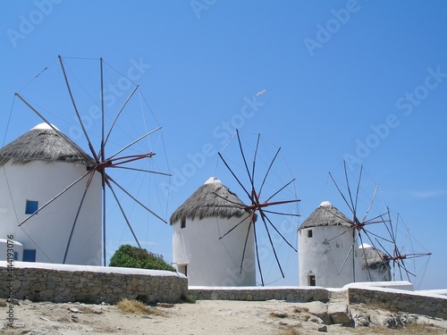  four of the famous white-washed mykonos windmills on the aegean sea on a sunny day on mykonos island, greece