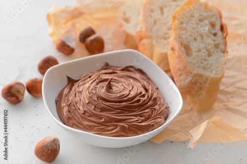 Bowl with tasty chocolate paste and hazelnuts on light background