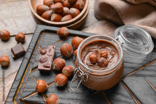 Jar with tasty chocolate paste and hazelnuts on wooden background