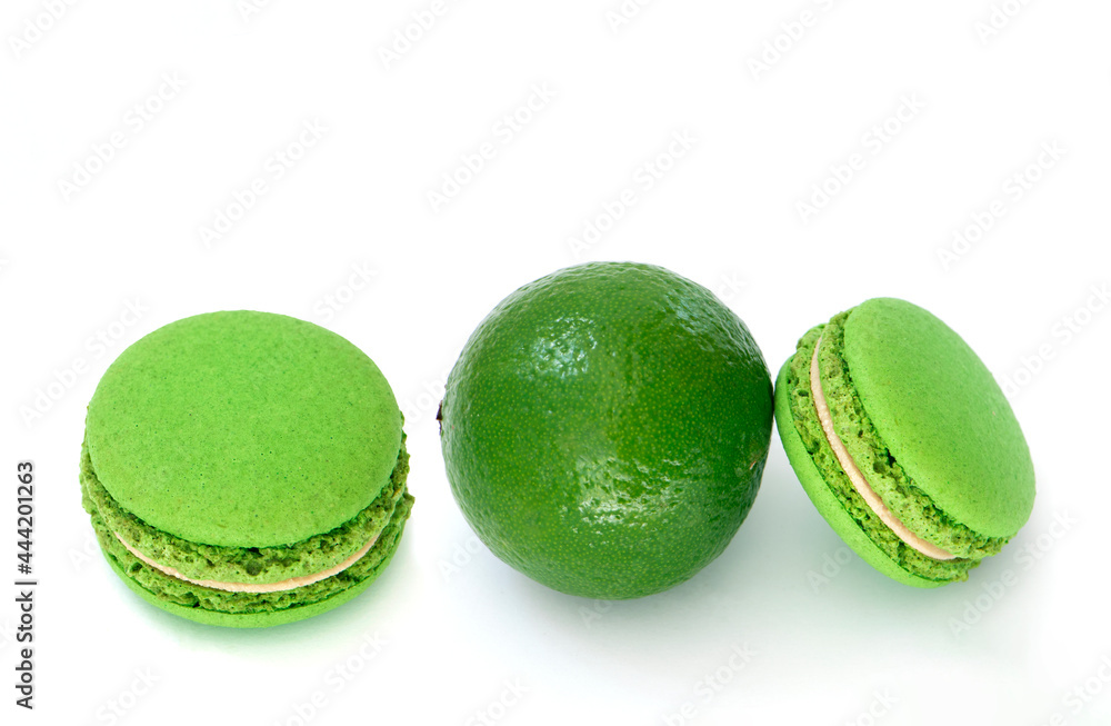 Green macaroon and fresh green lime on white background. High definition photo in close up. Lime macaroon cake isolated. Green dessert with pistachio flavor and green cream. High quality photo Green macaroon and fresh green lime on white background. High definition photo in close up. Lime macaroon cake isolated. Green dessert with pistachio flavor and green cream. High quality photo