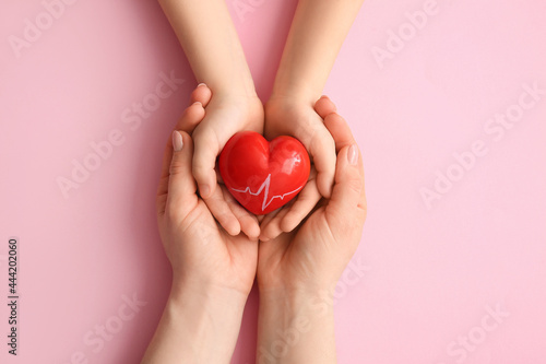 Fototapeta Naklejka Na Ścianę i Meble -  Hands of woman and child with red heart on color background