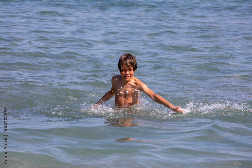 happy tanned boy splashes sea water in the sea, horizontal.