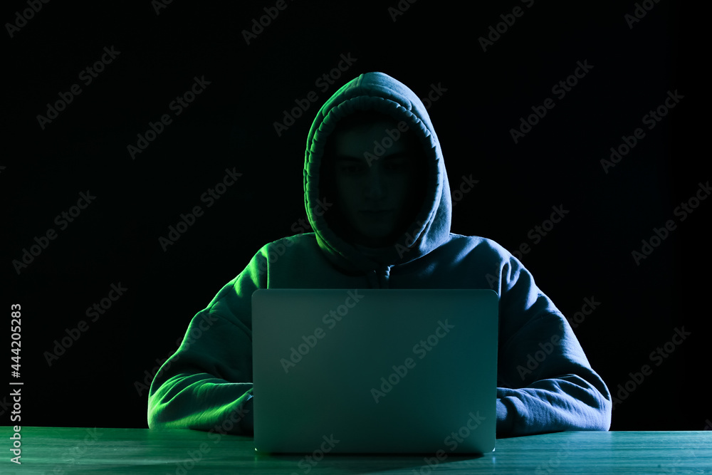 Silhouette of hacker with laptop at table on dark background Silhouette of hacker with laptop at table on dark background