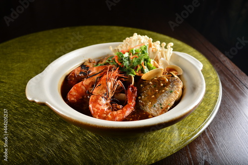 asian premium banquet menu braised seafood combo with big prawn , fish, shell and mushroom in hot clay pot on gold background dining table
