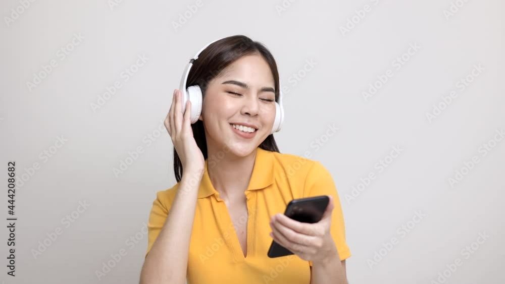 Beautiful young asian women choose song and play music from smartphone connection with wireless headphone having fun in home. Teenage girl listen to the music enjoy relaxing on isolated background. Beautiful young asian women choose song and play music from smartphone connection with wireless headphone having fun in home. Teenage girl listen to the music enjoy relaxing on isolated background.