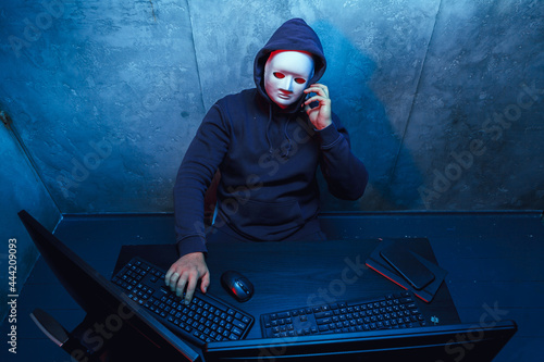 Anonymous hacker wearing face mask working on computer in dark room