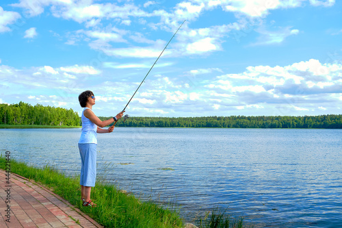 woman fishing on a spinning rod in the lake on summer day, outdoor activities, angler
