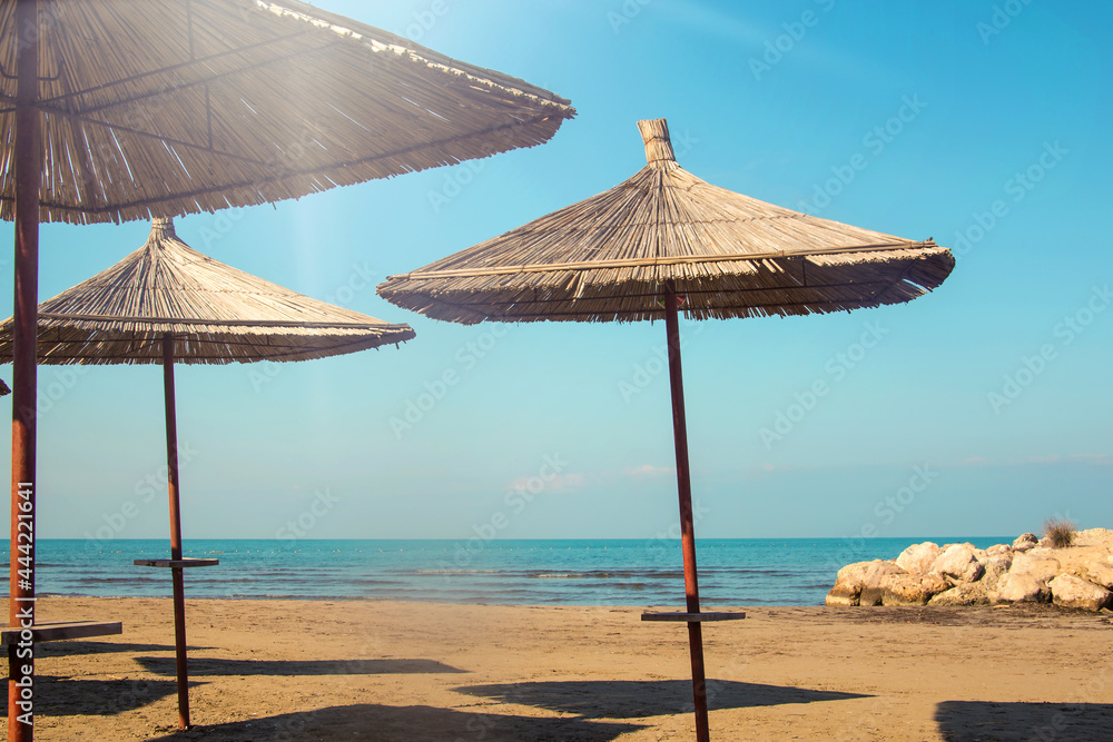 Fototapeta premium The beach of Albania, Durres. Umbrellas made of straw on a shoreline with the sea in the background.