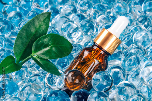 Mockup dropper bottle with natural organic herbal cosmetic oil on blue background of water gel balls. Trendy still life composition with copy space. Modern organic apothecary concept