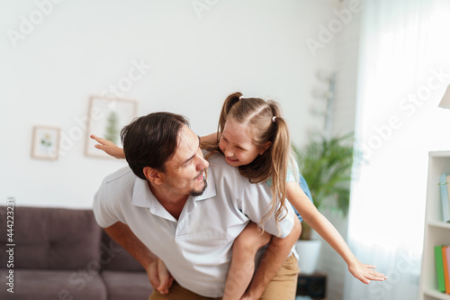 Happy positive cheerful dad is playing with his little charming daughter at home. The man circles and throws the girl up. A dynamic image. Copy space