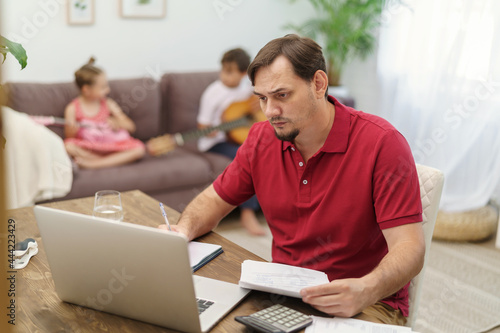 father works at home with a laptop together with the children. small children play the guitar, make noise and interfere with dad's work. a man tries to focus on remote work at home © skif