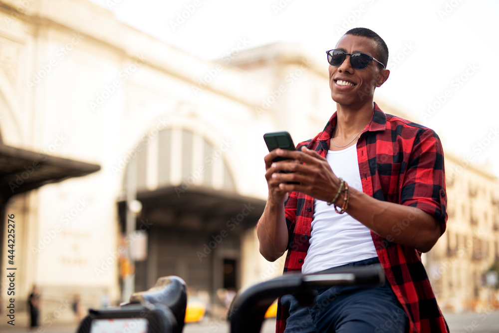 Portrait of handsome african man using electric bike in the city. Happy young man using the phone Portrait of handsome african man using electric bike in the city. Happy young man using the phone