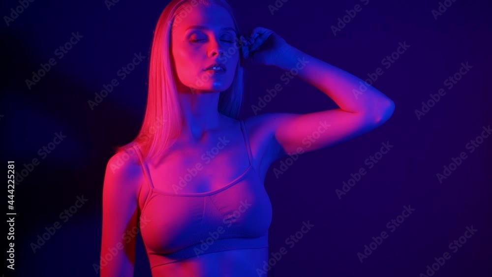 Beautiful model in lingerie poses in front of the camera in colored light. Neon light illuminates the face of a young blonde woman. Photo session and studio shooting in red and blue lights. Slow Beautiful model in lingerie poses in front of the camera in colored light. Neon light illuminates the face of a young blonde woman. Photo session and studio shooting in red and blue lights. Slow