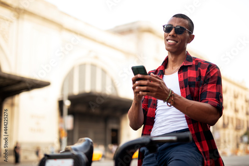 Portrait of handsome african man using electric bike in the city. Happy young man using the phone