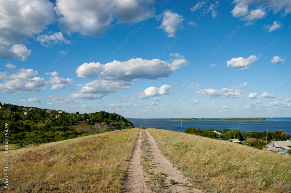 The road through the hill on the background of the Volga River and the cloudy sky. Beautiful weather and wildlife.