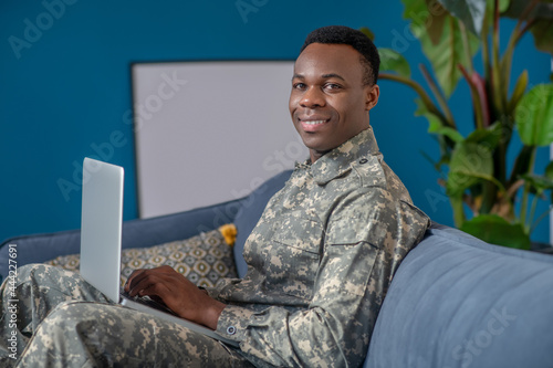 Happy confident military man with laptop on sofa