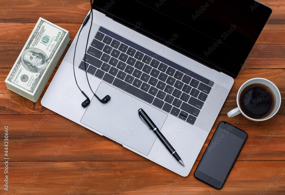 Topview or top down shot of laptop notebook computer with black coffee in white cup on wood background with pile of dollar money banknotes Topview or top down shot of laptop notebook computer with black coffee in white cup on wood background with pile of dollar money banknotes