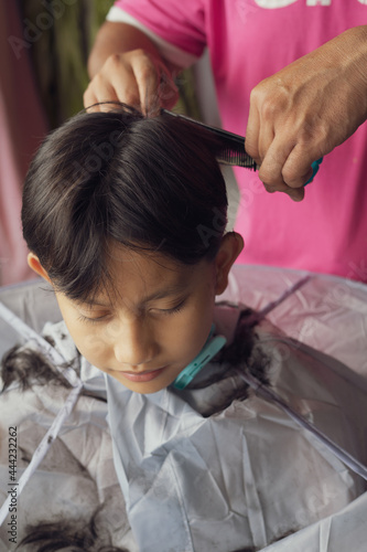 Asian young boy is getting haircut at home from the father.