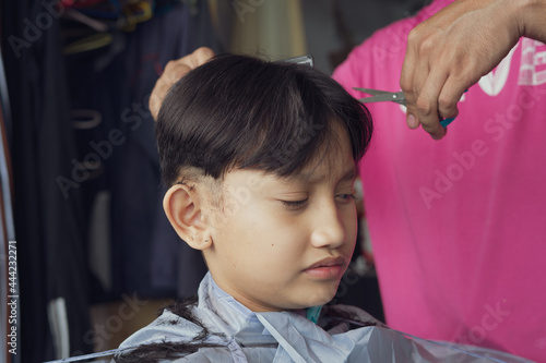 Asian young boy is getting haircut at home from the father.