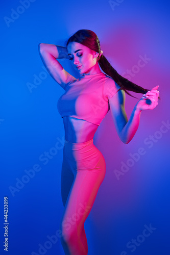 Slim body. Fashionable young woman standing in the studio with neon light