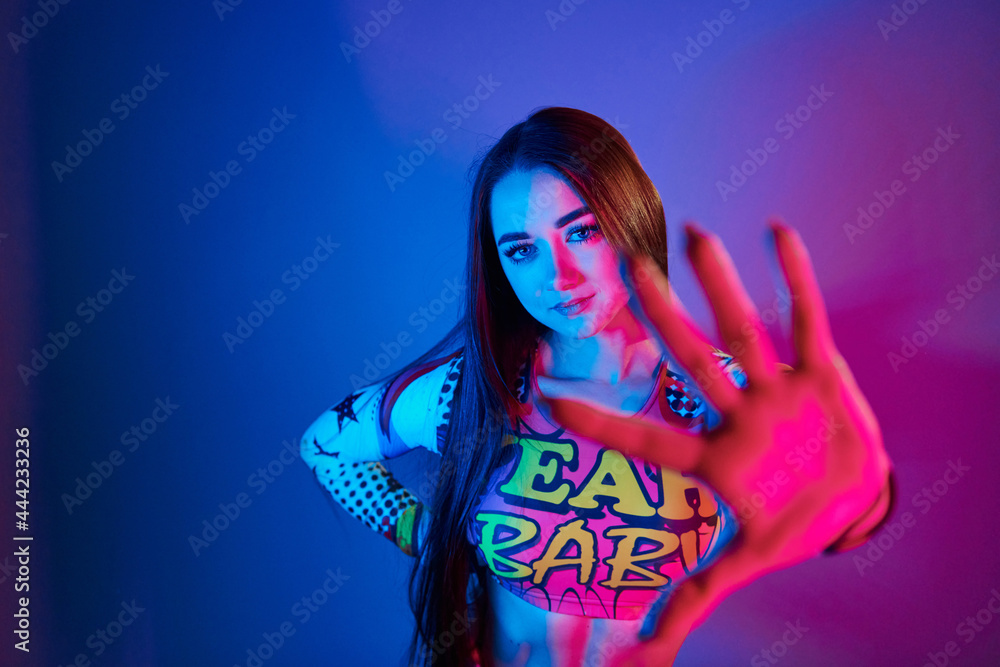 Stop, gesture. Fashionable young woman standing in the studio with neon light Stop, gesture. Fashionable young woman standing in the studio with neon light
