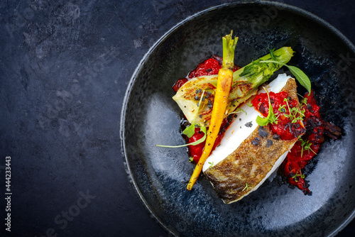 Modern style traditional fried skrei cod fish filet with fennel and tomato cream served as close-up in ceramic design bowl with copy space left