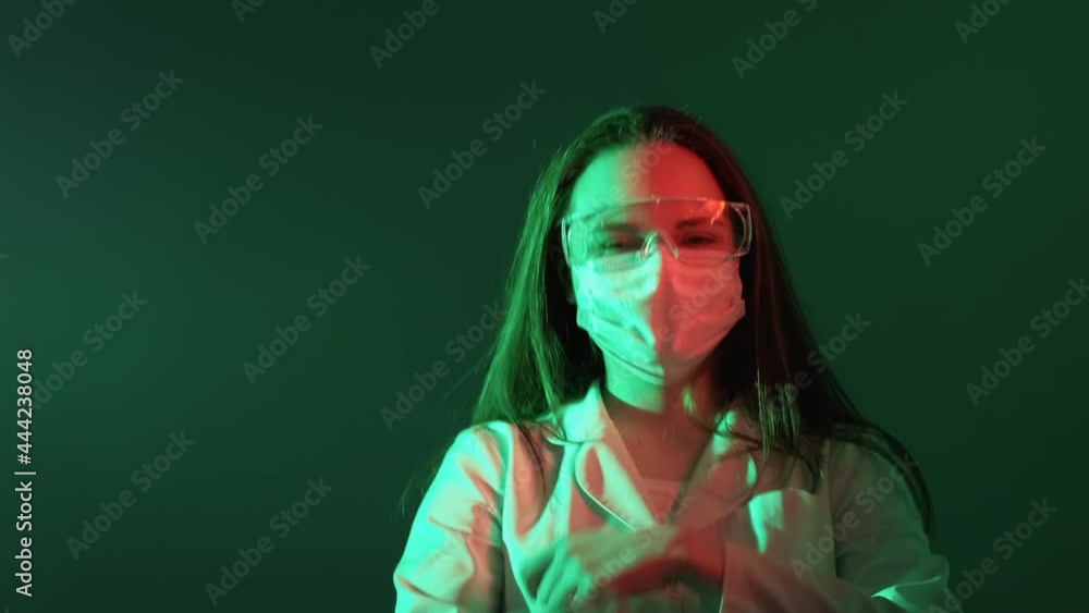 Satisfied doctor. Winner dance. Medical worker day party. Amused happy female surgeon in face mask celebrating victory in red green neon light isolated on teal copy space background. Satisfied doctor. Winner dance. Medical worker day party. Amused happy female surgeon in face mask celebrating victory in red green neon light isolated on teal copy space background.