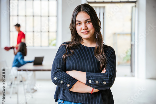 Portrait of a young female businesswoman with arms folded in her new office, behind her two colleagues working together - Successful millennial of a self-confident start-up - Concept of teamwork photo