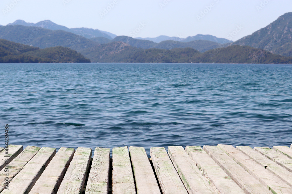 View from old wooden pier to deep blue water and misty mountains covered with forest. Beach vacation on the sea, background for summer vacation and travel