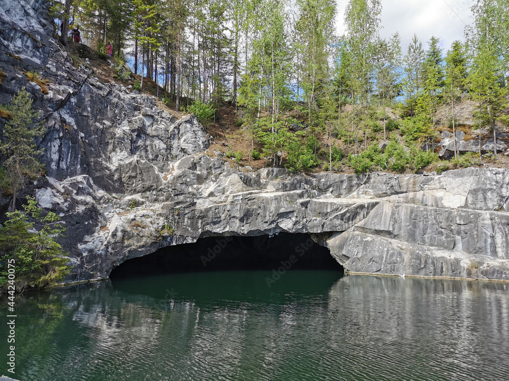 View from the water of the grotto and the slope of the flooded Marble Canyon, where trees grow, in the mountain park Ruskeala on a sunny summer day.