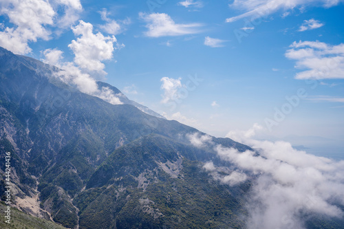 Sunny day high in the mountains, mountain peaks, blue sky, clouds on the tops of mountains, rocks, sharp peaks and steep mountain slopes
