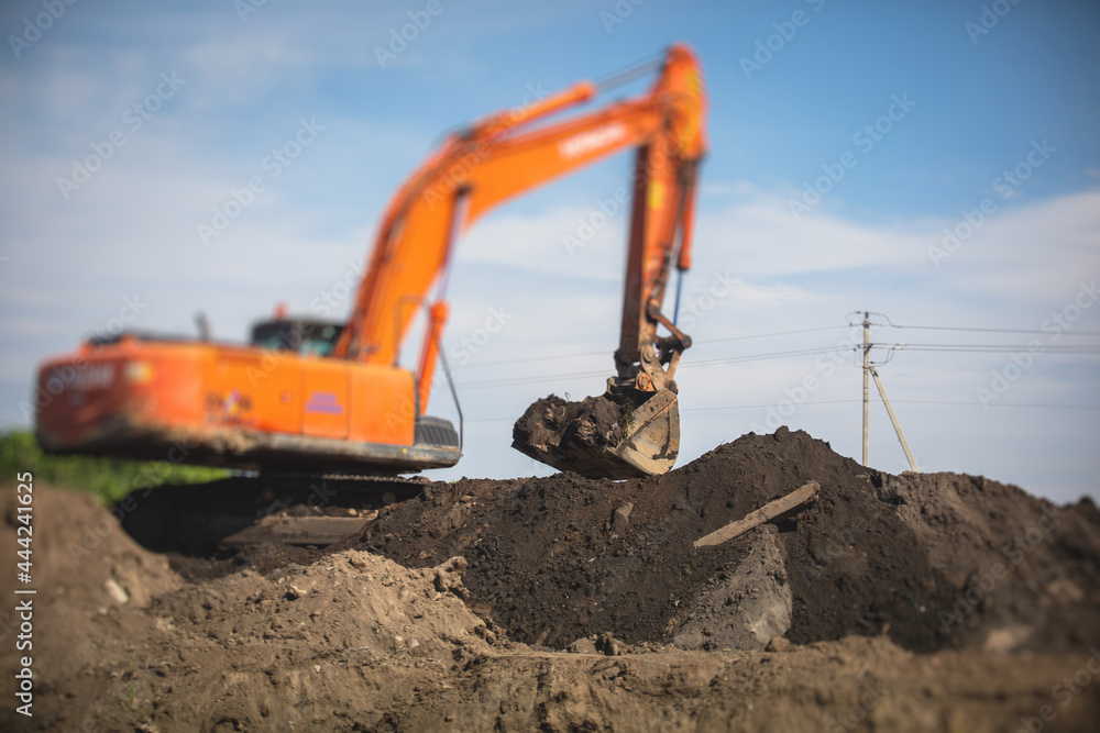 Yellow heavy excavator and bulldozer excavating sand and working during road works, unloading sand during construction of the new road Yellow heavy excavator and bulldozer excavating sand and working during road works, unloading sand during construction of the new road