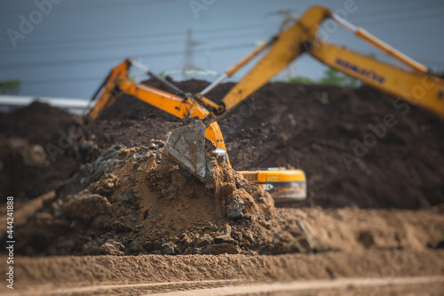 Yellow heavy excavator and bulldozer excavating sand and working during road works, unloading sand during construction of the new road