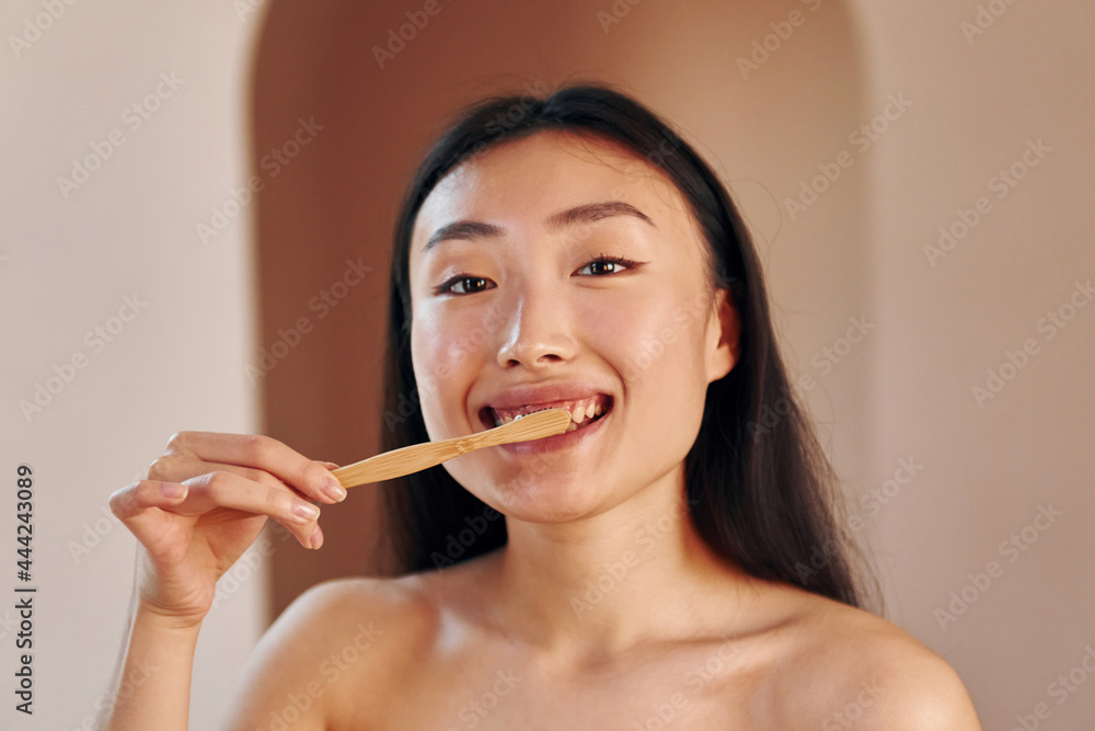 Holds toothbrush. Young serious asian woman standing indoors Holds toothbrush. Young serious asian woman standing indoors