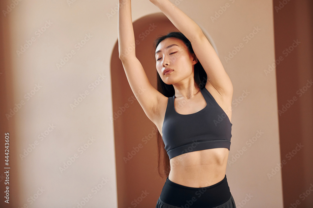 Doing fitness exercises. Young serious asian woman standing indoors
