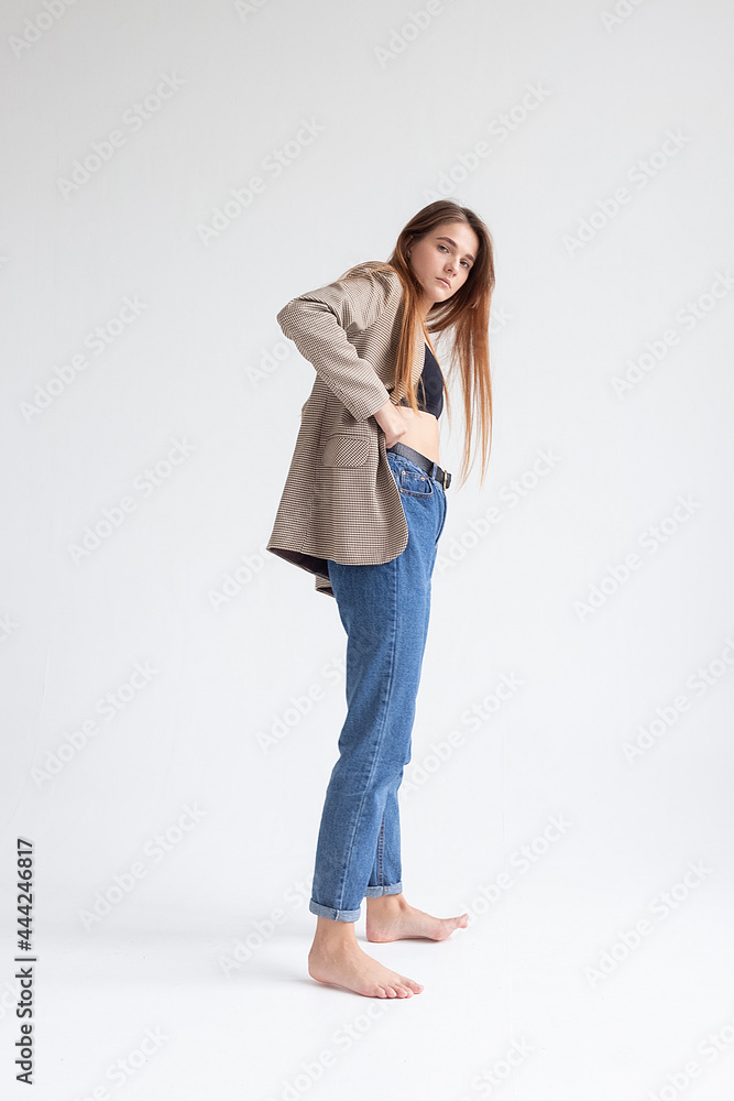 portrait of young caucasian attractive woman with long brown hair in blue jeans, black top and suit jacket on white background. skinny pretty lady posing at studio with bare feet portrait of young caucasian attractive woman with long brown hair in blue jeans, black top and suit jacket on white background. skinny pretty lady posing at studio with bare feet