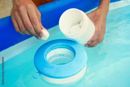 Hand holding white chlorine tablets over swimming pool skimmer. Chlorination of water in pool for disinfection and prevention against the development of microbes. photo
