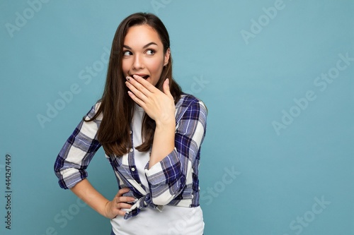 Photo of young positive happy shocked attractive pretty brunet woman with sincere emotions wearing stylish check shirt standing isolated on blue background with empty space