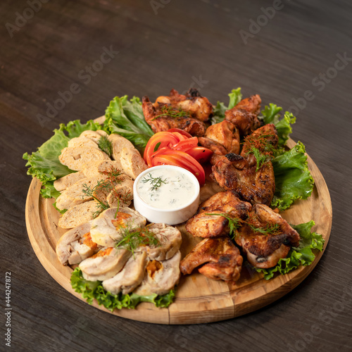 Meat appetizer. Pieces of baked meat and friesh lettuce leaves on wooden cutting board with mayonnaise sauce in center of it. Copy space. Soft focus. photo