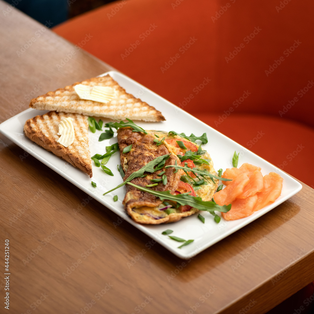 Slices of red fish, omelet with arugula and toast with butter on white platter. Morning mood, breakfast. Soft focus. Copy space.