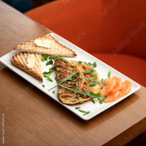 Slices of red fish, omelet with arugula and toast with butter on white platter. Morning mood, breakfast. Soft focus. Copy space.