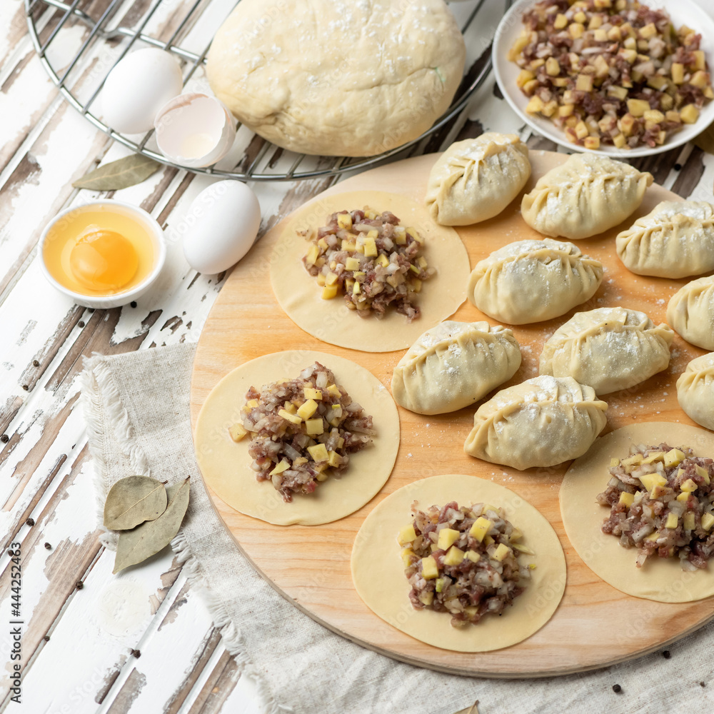 Cooking process. Dumplings stuffed with minced meat and cheese. Convenience Food. Raw dough slices with filling on rustic wooden table. Top view. Square format. Soft focus. Cooking process. Dumplings stuffed with minced meat and cheese. Convenience Food. Raw dough slices with filling on rustic wooden table. Top view. Square format. Soft focus.