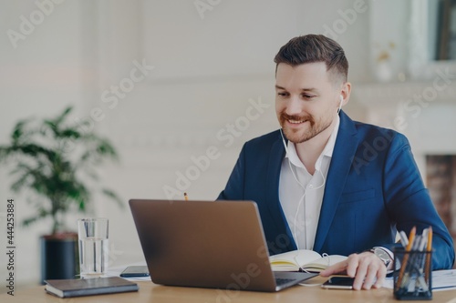 Smiling executive manager wearing earphones having online meeting with employees