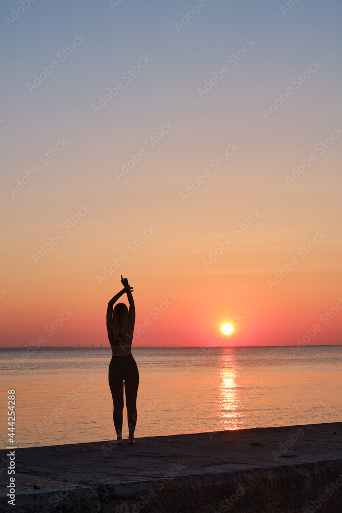 A woman is engaged in meditation near the sea on the pier. Sunrise Meditation. Healthy lifestyle, active rest. Morning yoga near the sea. Tourism, travel and yoga concept