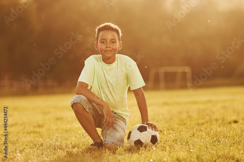 Sits with soccer ball. African american kid have fun in the field at summer daytime © standret