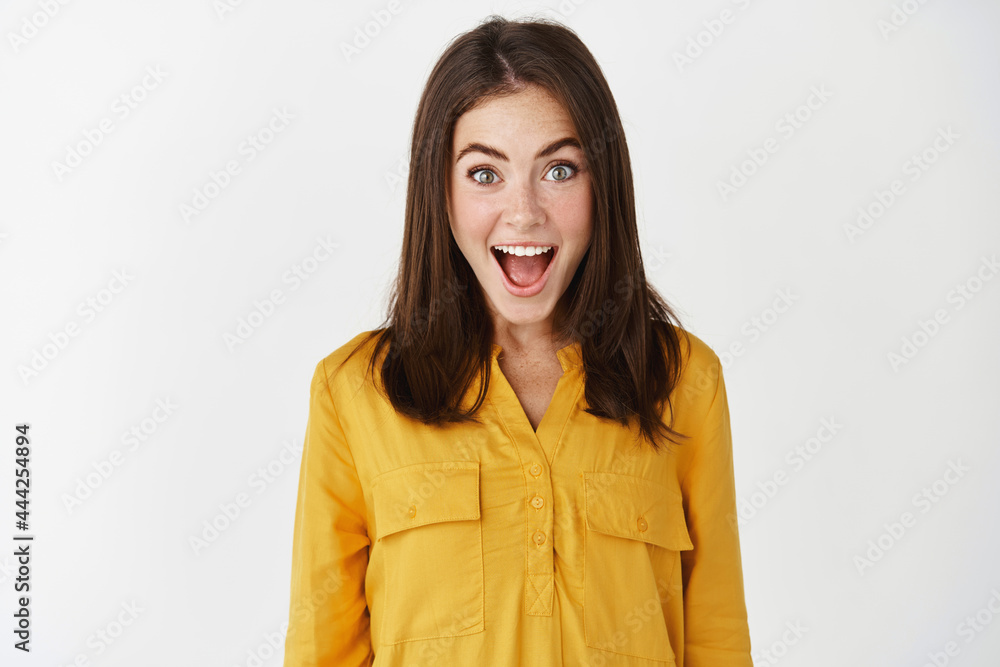 Close-up of happy and surprised woman open mouth and staring with disbelief, receive good news, express amazement while standing over white background Close-up of happy and surprised woman open mouth and staring with disbelief, receive good news, express amazement while standing over white background